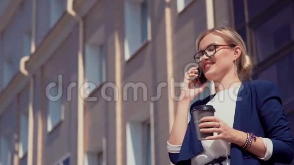 一个嘴唇和眼镜上涂着红色口红的年轻女孩站在阳光明媚的街道上的一栋办公楼附近女孩视频的预览图