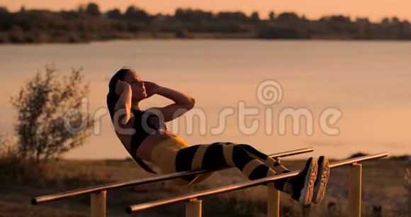 腹部肌肉锻炼日落时分一位年轻的美女在湖边运动一位穿着运动服的夏日女子在做运动视频的预览图