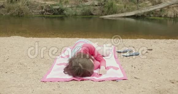 年轻女孩穿着五颜六色的泳装在河滩晒日光浴视频的预览图
