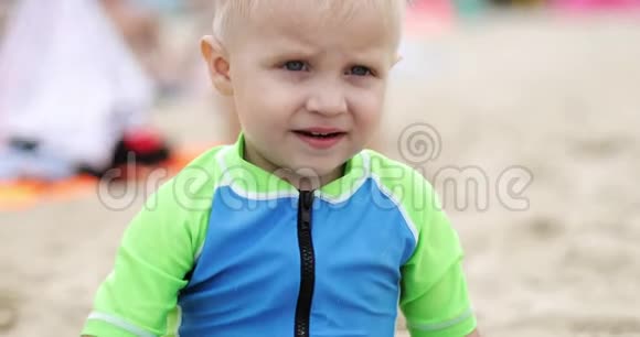 一个可爱的金发男孩坐在海滩上的肖像视频的预览图