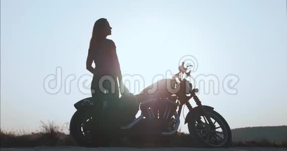 退休女孩站在摩托车旁边在背光下欣赏日落视频的预览图