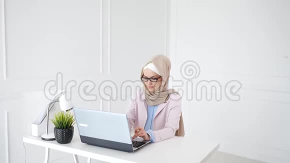 美丽的年轻穆斯林妇女正在工作场所的笔记本电脑上工作视频的预览图