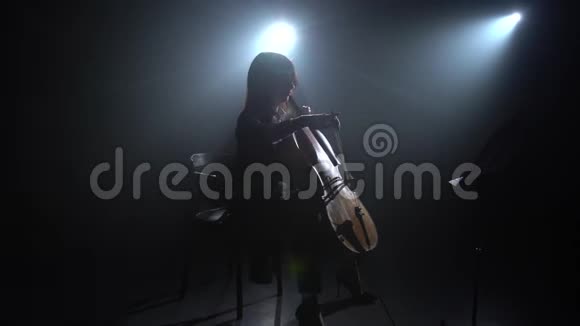 在黑暗的工作室里女人的手在大提琴上打弓剪影黑烟背景视频的预览图