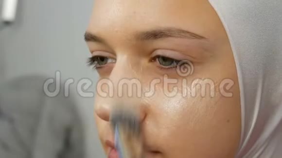 一个专业的化妆师用特殊的画笔将遮瑕膏应用于女孩模型高级时尚拍摄视频视频的预览图