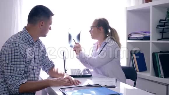 医生拿着笔记本电脑和x光坐在桌子旁说坏消息然后在医疗办公室支持病人视频的预览图