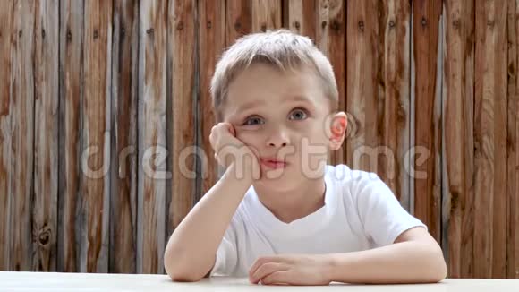 一个恶毒的孩子男孩坐在桌子旁把头放在手上孩子思考和梦想视频的预览图