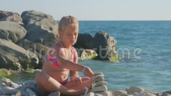 小女孩在海边的海滩上建了一座鹅卵石塔孩子梦想的概念视频的预览图