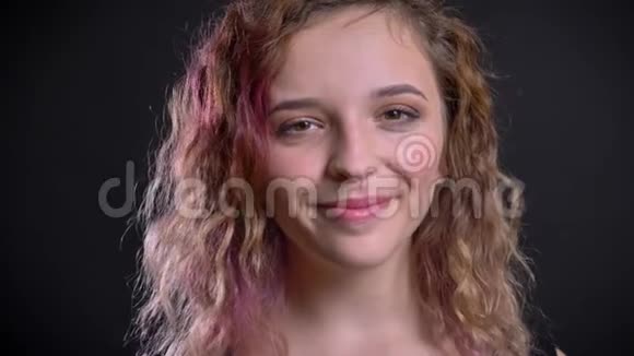年轻的白种人女孩的肖像粉红色的头发看着镜头谦逊地微笑在黑色的背景视频的预览图