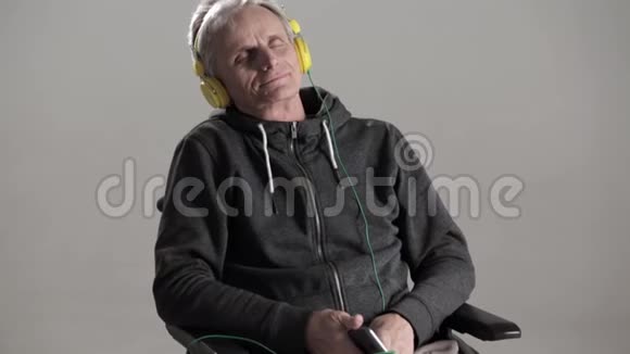 一个戴着灰色头发的人坐在轮椅上听着最喜欢带耳机的音乐视频的预览图