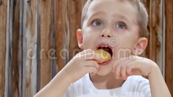 一个孩子在木墙的背景下坐在一张桌子旁一边高兴地吃薯片特写镜头视频的预览图