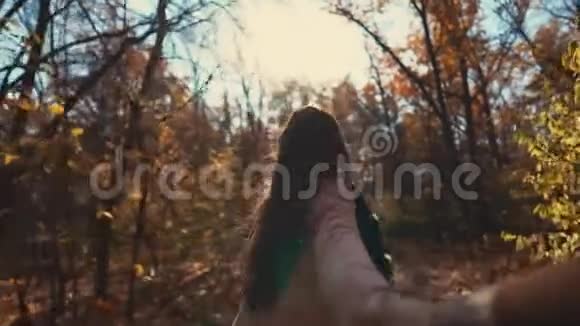 男人正在拍摄他的女朋友牵着他的手在秋天阳光明媚的森林里奔跑视频的预览图