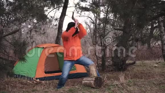 一个穿着明亮夹克和冬帽的旅行者在一个旅游帐篷的背景上生火砍柴视频的预览图