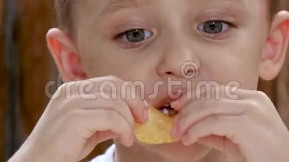 孩子坐在木墙背景的桌子旁吃薯片特写镜头视频的预览图