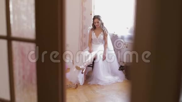 美丽可爱的新娘穿着婚纱坐在椅子上看着她的鞋子猫坐在女人旁边婚礼早视频的预览图