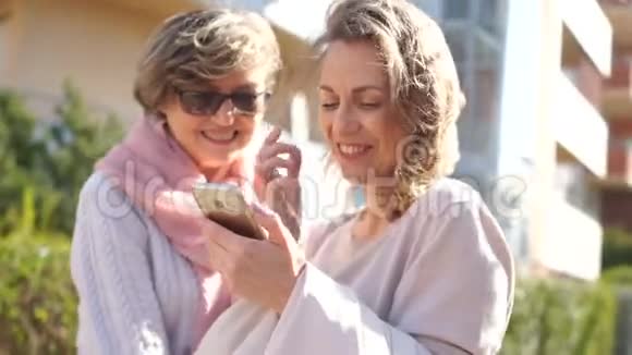 两个手里拿着智能手机的女人的欢快画像母女俩笑着站在中间视频的预览图
