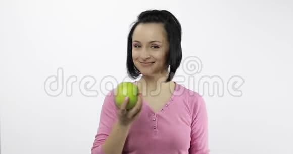 年轻漂亮的女人在白色背景下吃着大而多汁的绿苹果视频的预览图
