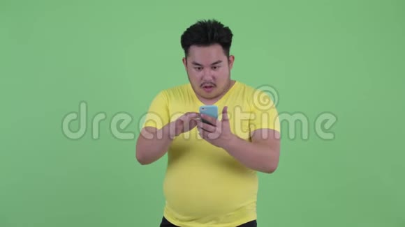 快乐的年轻超重的亚裔男子使用电话得到好消息视频的预览图