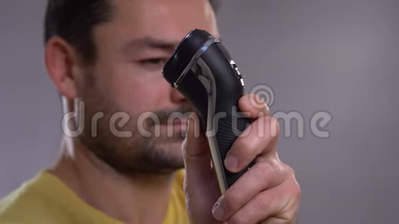 一个用电动剃须刀刮胡子的年轻人的特写视频的预览图