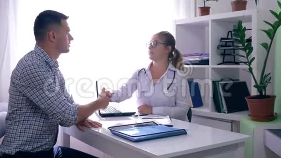 医生端着笔记本电脑和x光坐在桌子旁给办公室里的病人讲个好消息视频的预览图