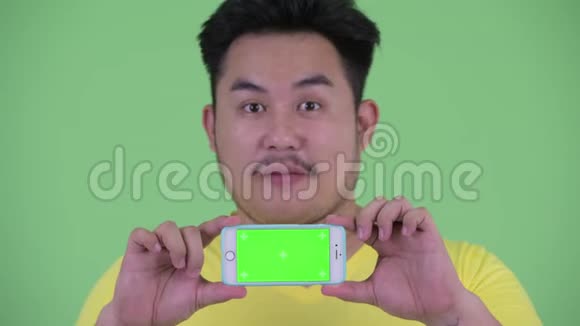 一个快乐的年轻的体重超重的亚洲男人一边看着电话一边思考视频的预览图