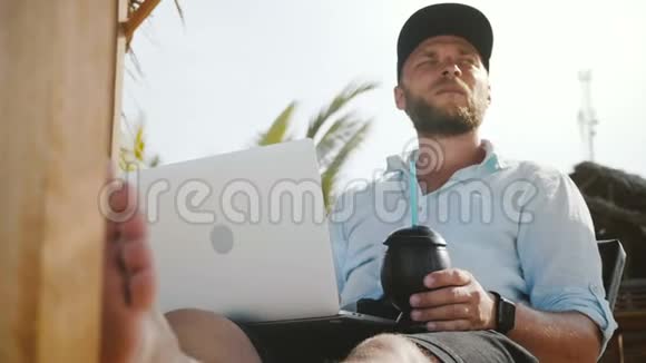 低角度拍摄成功的快乐轻松商人与笔记本电脑和饮料休息在海滩躺椅度假视频的预览图