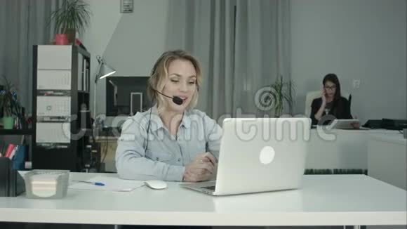 微笑呼叫中心操作员使用办公室耳机与笔记本电脑工作视频的预览图