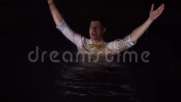 一个年轻人穿着衬衫和其他衣服在游泳池里洗澡晚上在热带别墅聚会喝醉了洗澡视频的预览图