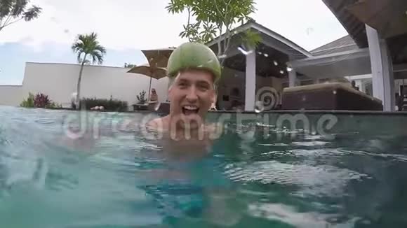 一个戴着西瓜头盔的年轻人在聚会上在游泳池里玩热带别墅度假视频的预览图