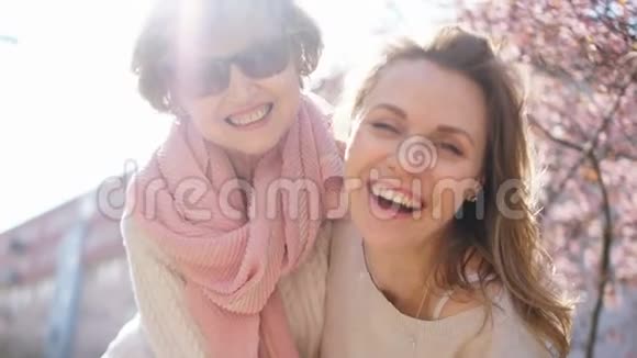 一位成年妇女和她的母亲在樱花灿烂的阳光和春天的花朵的背景下拥抱关闭视频的预览图