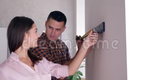 已婚夫妇在住宿修理期间用卷尺把架子挂在墙上视频的预览图