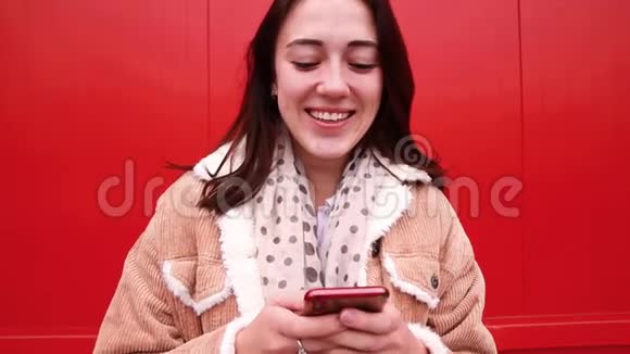 一位年轻的女博主站在红墙前看着手机的屏幕录制视频视频的预览图