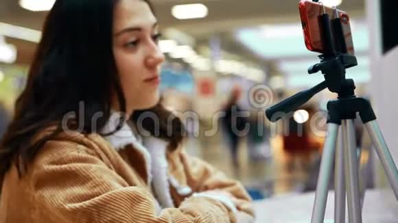 一位年轻的女博主站在红墙前看着手机的屏幕录制视频视频的预览图