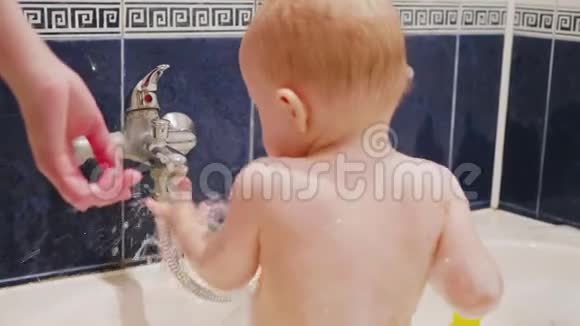 小男孩在洗澡时笑着玩水流妈妈的手在他身边慢动作中视频的预览图