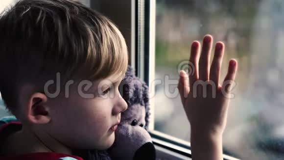 小男孩悲伤地盯着窗外怀里抱着一只泰迪熊坐在窗台上那孩子望着窗外视频的预览图