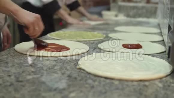 一群厨师把酱汁均匀地放在面团的圆圈上做披萨视频的预览图