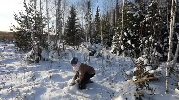 一个年轻女孩把雪洒在自己身上冬天阳光明媚的乐趣场景背景下的一片雪林视频的预览图