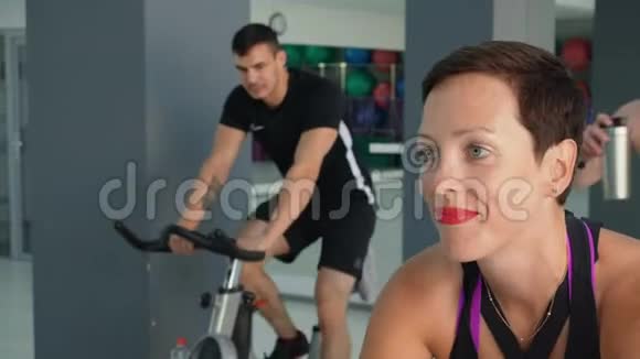 微笑的女人在自行车课上训练静态自行车肖像适合妇女在健身房自行车训练团体运动员视频的预览图