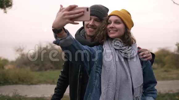快乐的年轻夫妇在秋天公园用手机自拍戴着黄色帽子的女孩拿着智能手机美丽美丽视频的预览图