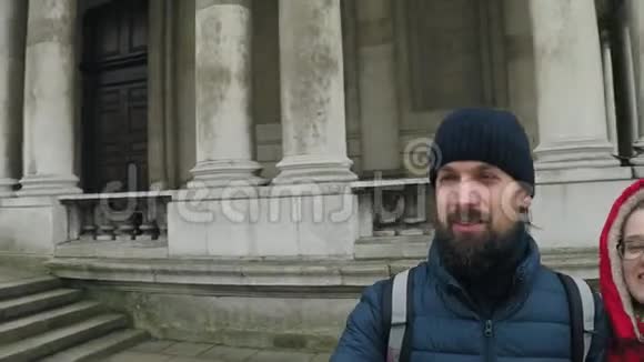 一个戴着深蓝色帽子和夹克留着胡子和长发的人在伦敦的一个公园里散步公园里有一栋柱廊建筑视频的预览图