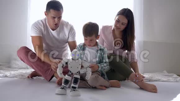现代童年可爱的孩子和父母玩智能机器人遥控手机坐在地板上视频的预览图