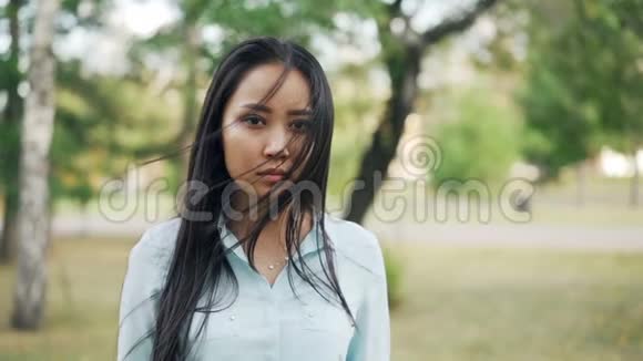 美丽的亚洲女人的慢镜头肖像黑眼睛黑发穿着时髦的衬衫站在户外微笑着视频的预览图