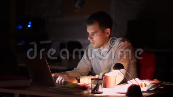 办公室里漆黑一片白种人正在电脑旁工作脸上的光从屏幕上亮起一边喝着视频的预览图