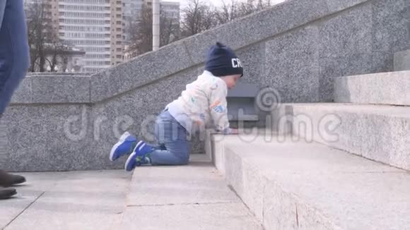 小男孩正在城市公园的花岗岩楼梯上爬他父亲把孩子扶起来帮助他度过一个阳光明媚的日子视频的预览图