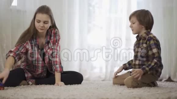 肖像姐姐和弟弟一起玩坐在地板上毛茸茸的地毯上那个男孩在玩视频的预览图