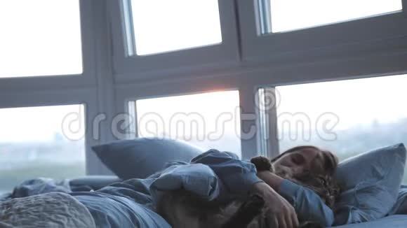 美丽的黑发女人躺在床上和她的缅因州考恩猫睡在房间的全景窗口慢慢慢慢视频的预览图