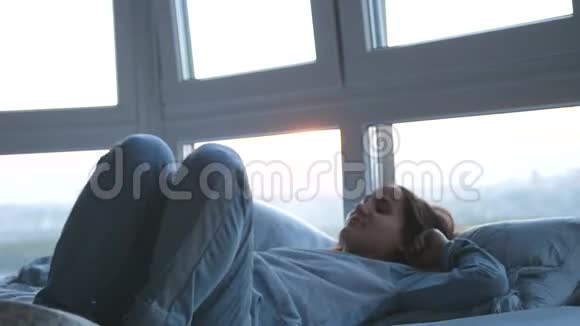 美丽的黑发女人躺在床上睡在房间的全景窗口慢动作视频的预览图