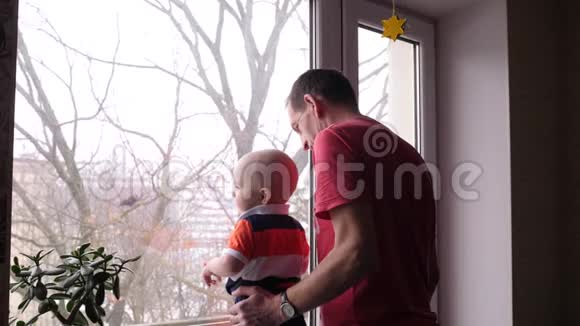 一位老人和他可爱的小孙子在窗边玩耍男孩抚摸着站在窗户上的花视频的预览图