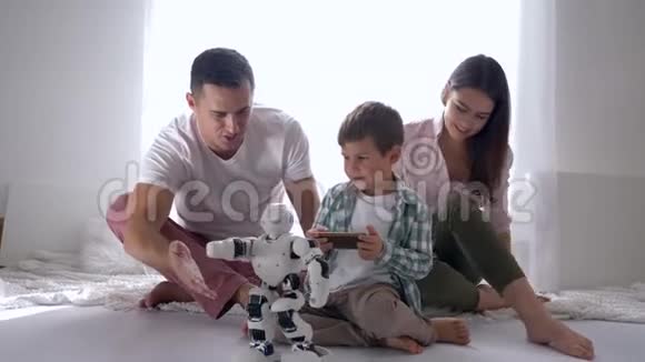 现代玩具小男孩和爸爸妈妈一起玩人形机器人遥控智能手机坐在地上视频的预览图