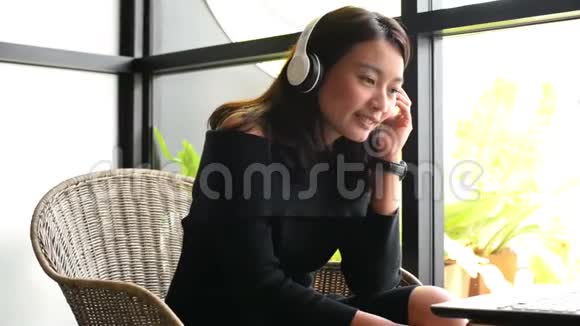 亚洲女性在城市咖啡店使用笔记本电脑和耳机听音乐视频的预览图