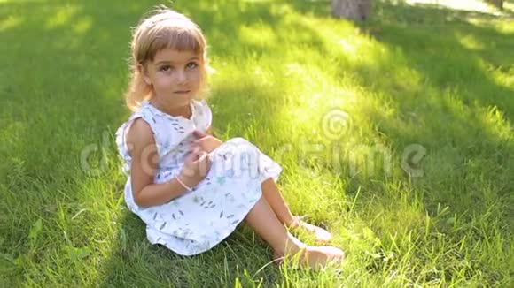 穿着夏装的小女孩和坐在公园绿草上的发箍视频的预览图